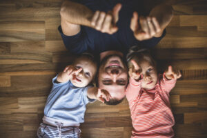 father-and-children-lying-on-floor-with-hands-raised_23-2147615917
